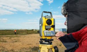 A licensed land surveyor using equipment to measure property boundaries on a development site for a boundary line survey