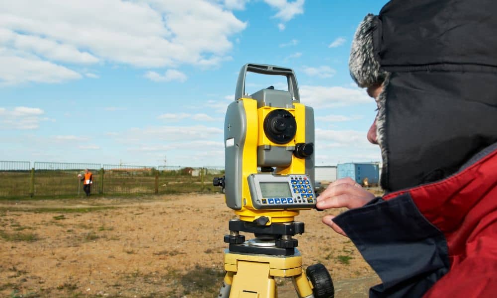 A licensed land surveyor using equipment to measure property boundaries on a development site for a boundary line survey