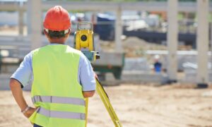 A commercial property surveyor measuring land at a construction site with equipment in use