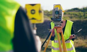 Surveyor using a total station during a topographic survey in tall grass field