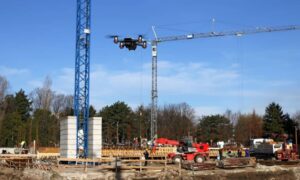 Professional drone surveying an active construction site with cranes and workers, collecting aerial data for engineering and land surveying projects.