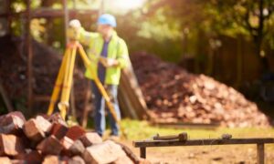 Land surveyor using tripod equipment during a flood elevation survey at a residential property site